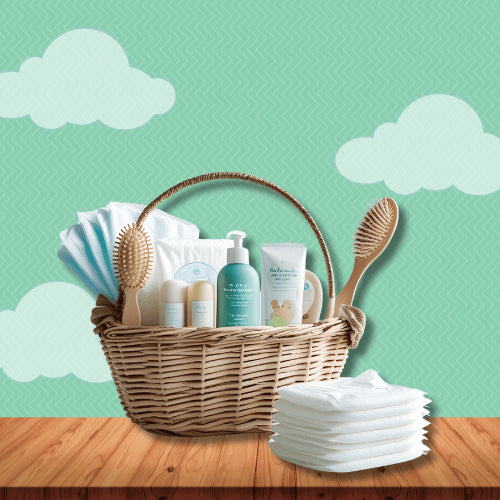 Newborn essentials basket including baby wipes, shampoo, lotion, soft brushes and diapers in wicker basket for gifting.
