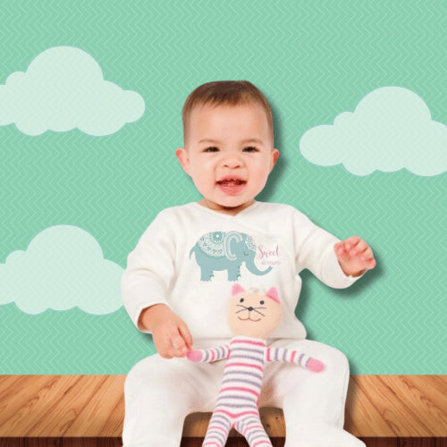 Happy baby wearing elephant onesie and holding soft pink striped stuffed toy, seated against playful sky-themed backdrop.