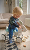 Toddler riding a wooden bunny-shaped toy bike while playing with wooden blocks on the floor.